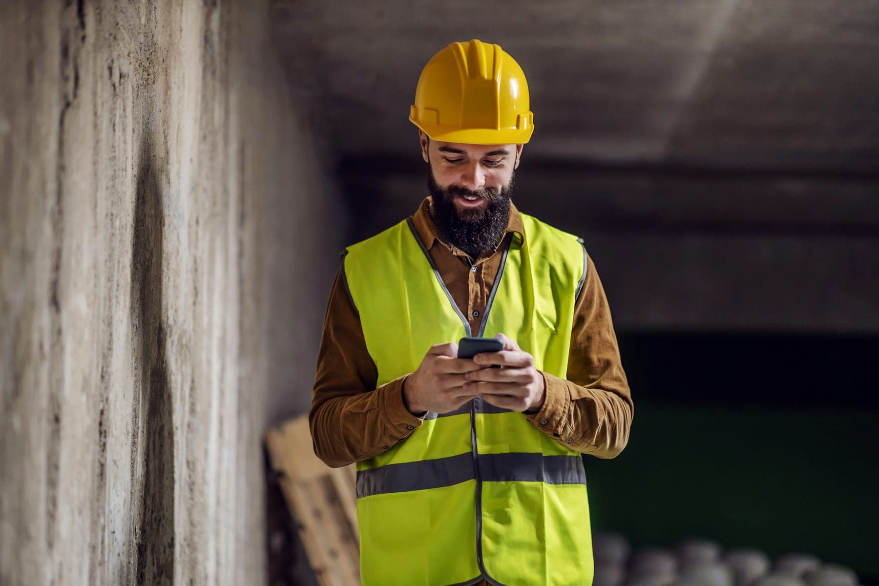 Tradesman in a hi-vis vest smiling at his phone on a building site